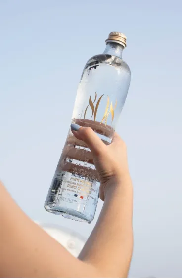 Bouteille en verre d’eau minérale naturelle 808 Naturelle plate tenue à la main sur fond de ciel