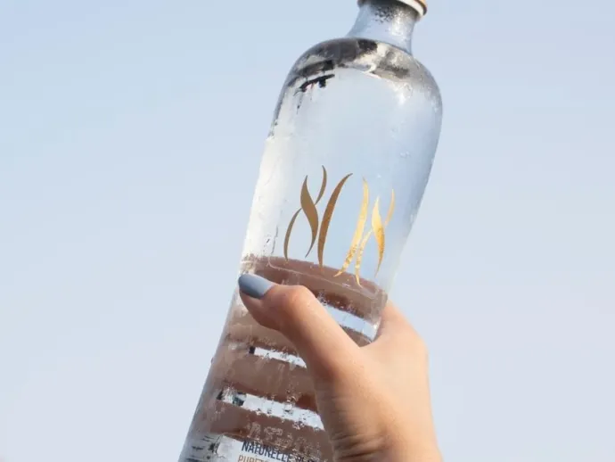 Bouteille en verre d’eau minérale naturelle 808 Naturelle plate, logo doré, tenue face au ciel